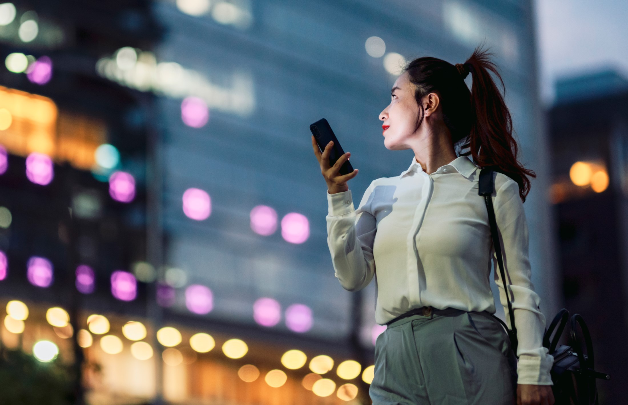 Woman in an urban environment holding a mobile phone in her hand.