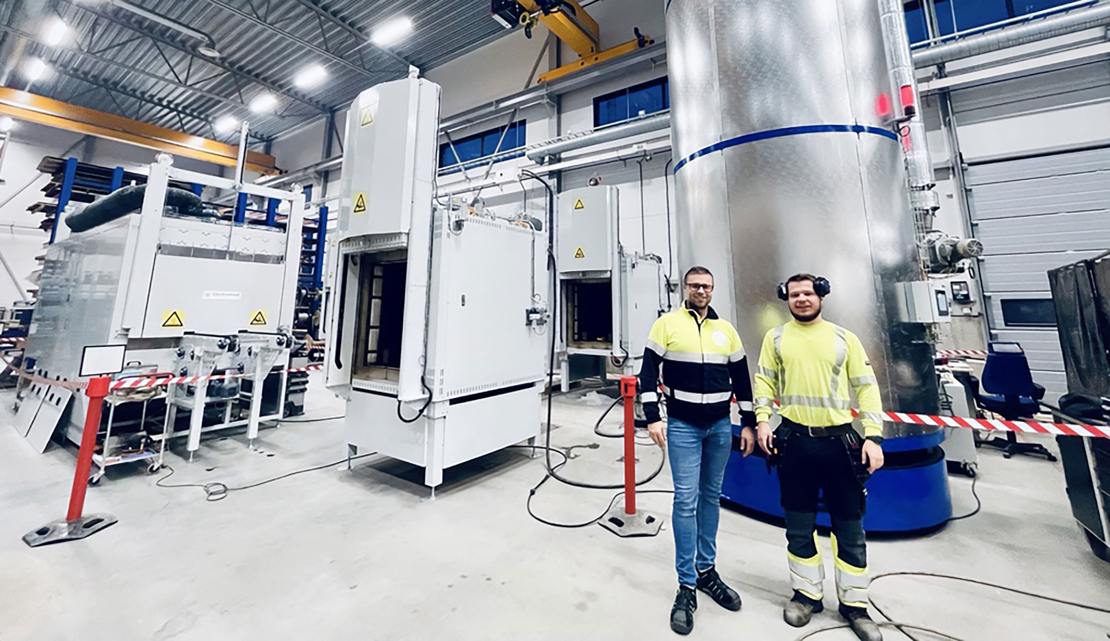Två män i varselkläder står framför ElectroHeats produkter i industrimiljö.