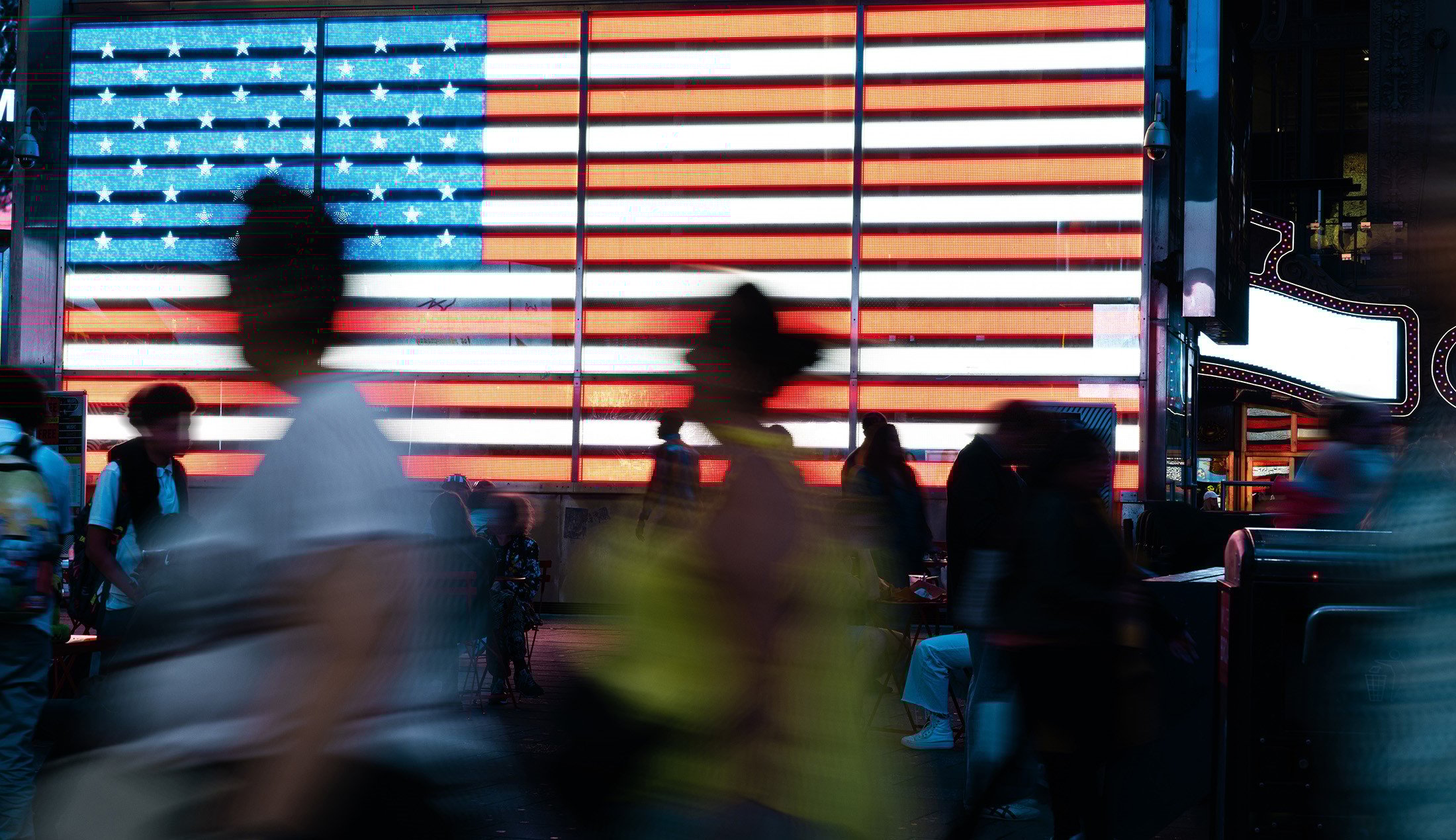 Folk skyndar förbi en stor ljusskylt med amerikanska flaggan.