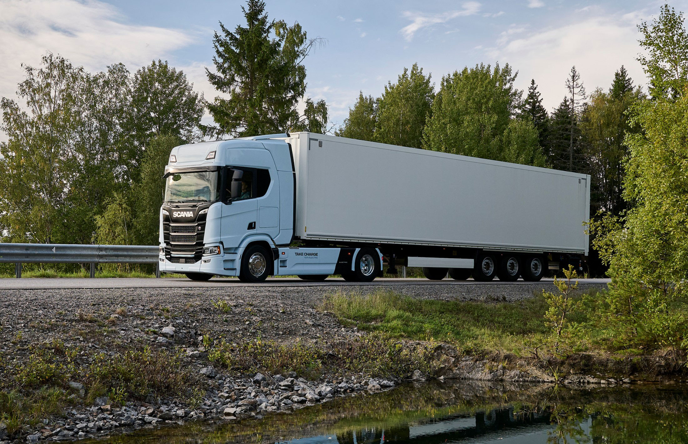 A Scania truck on a road surrounded by trees.