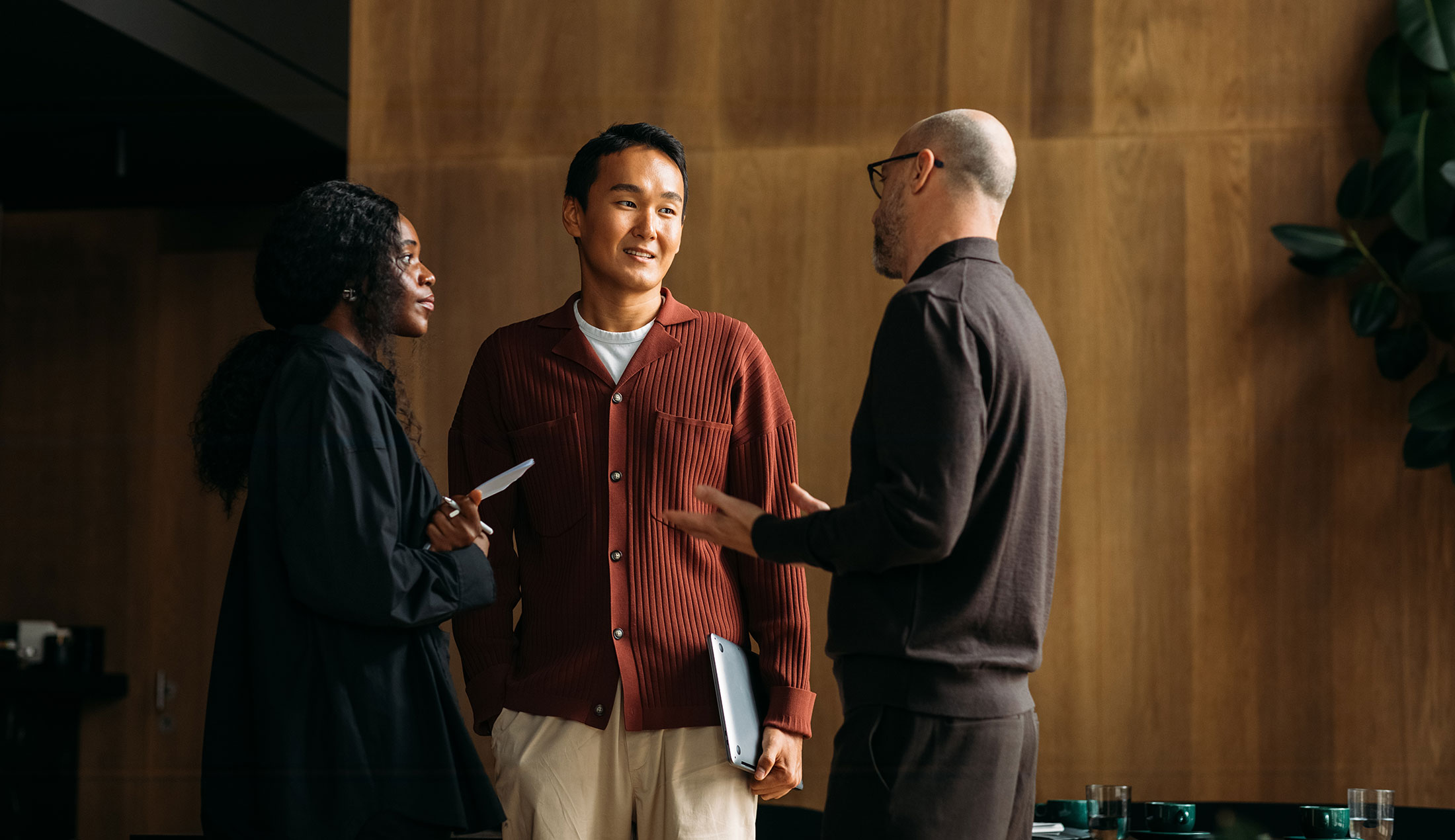 A woman and two men standing and talking in an office environment.