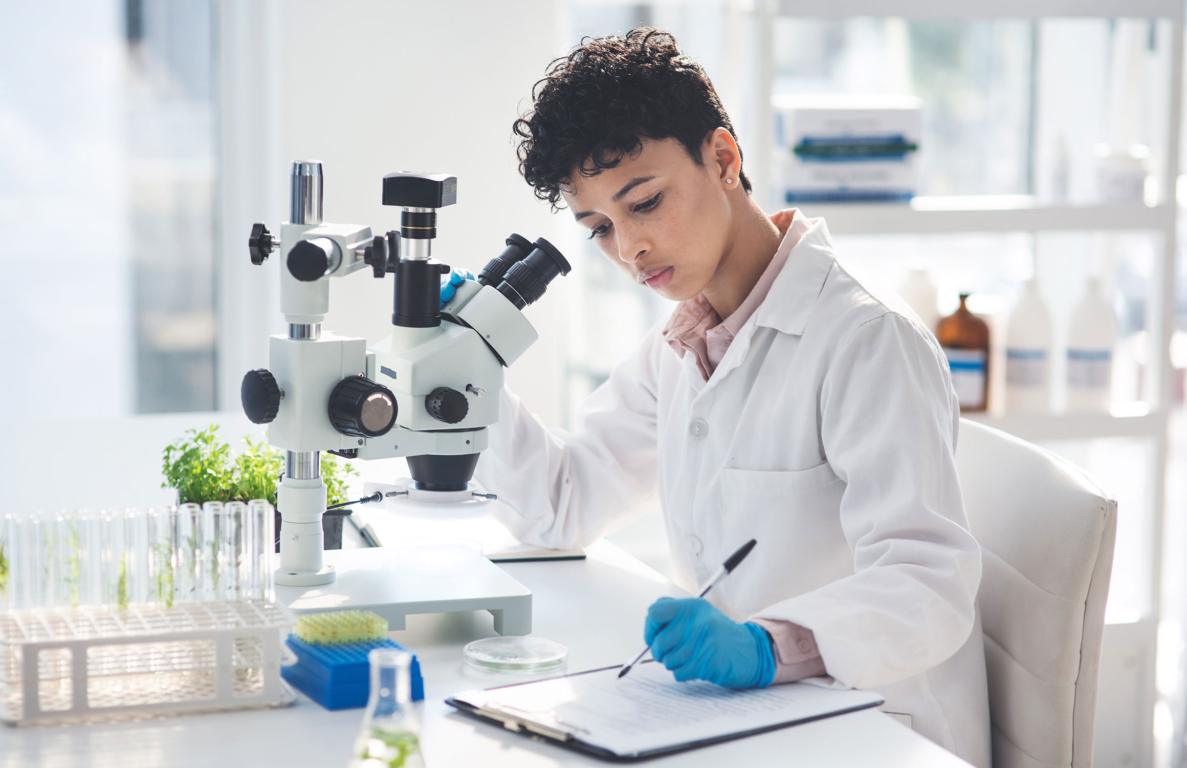 Woman working with a microscope in a lab, taking notes.