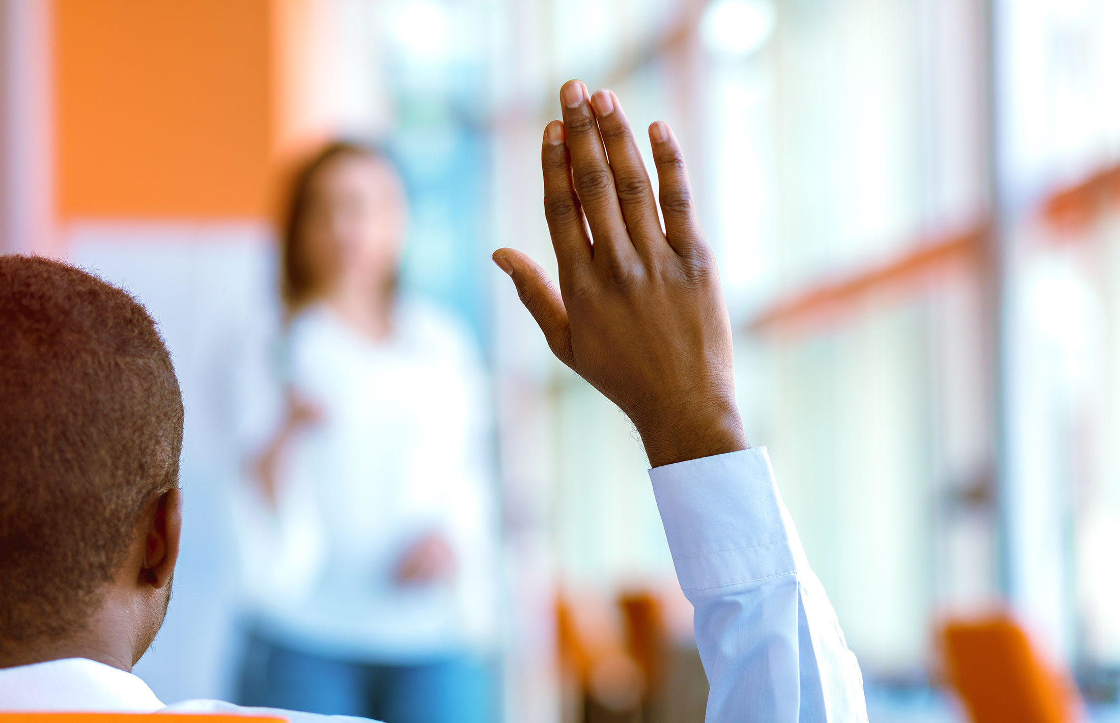 A man sitting with his back to the camera raises his hand to ask a question.