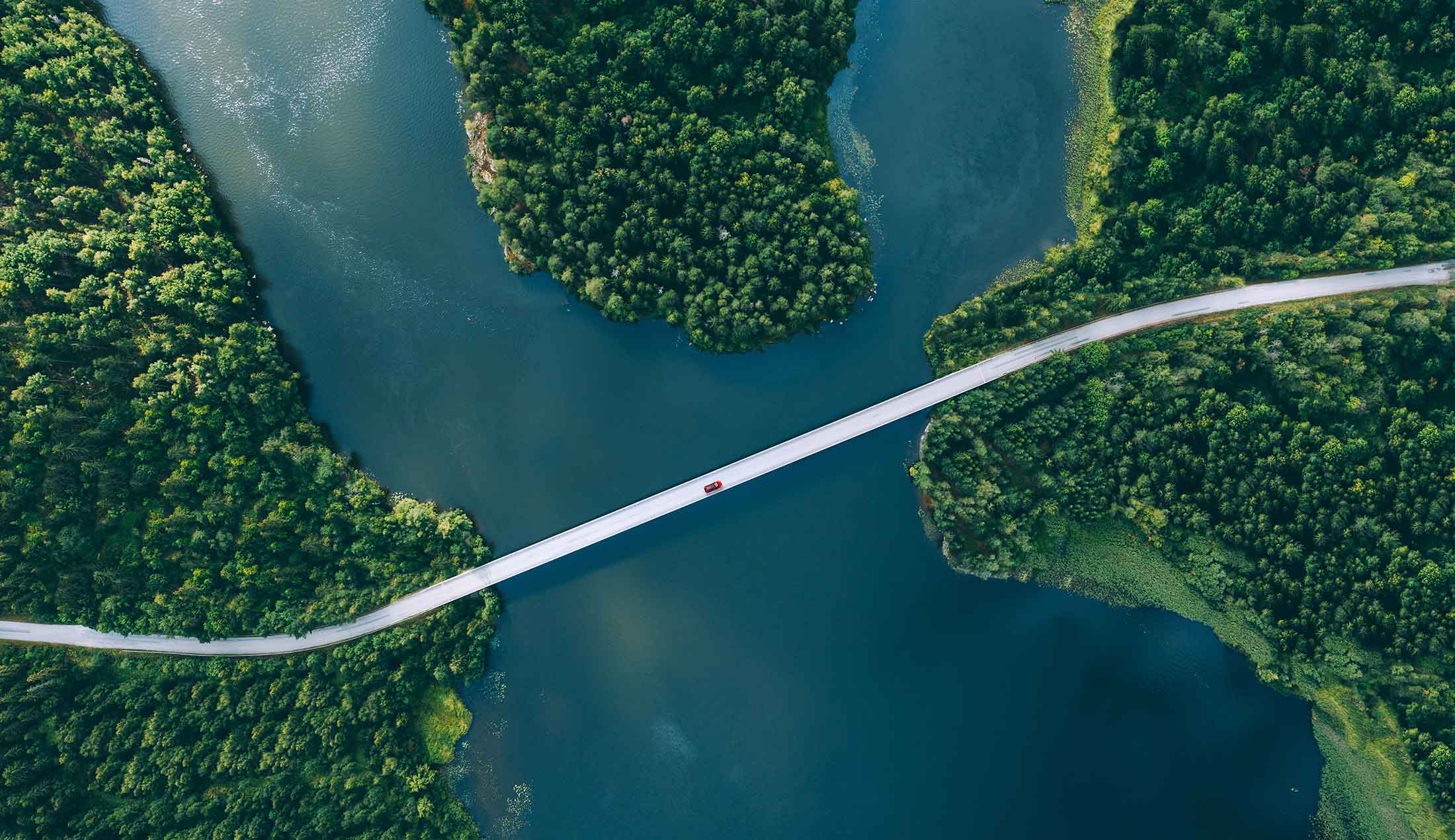 Flygbild på en väg som slingrar sig genom skog och över vatten