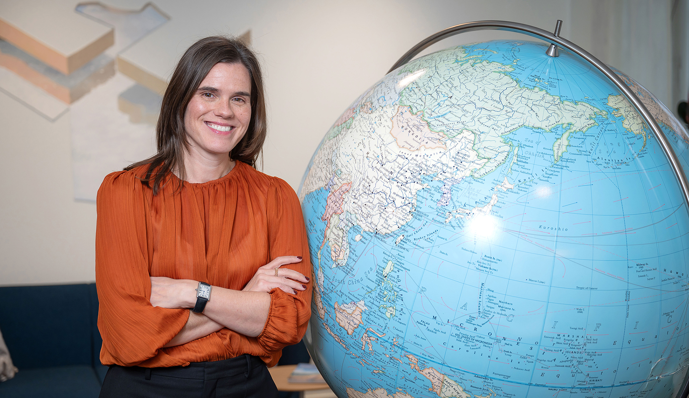 A young woman stands beside a large globe, smiling at the camera.